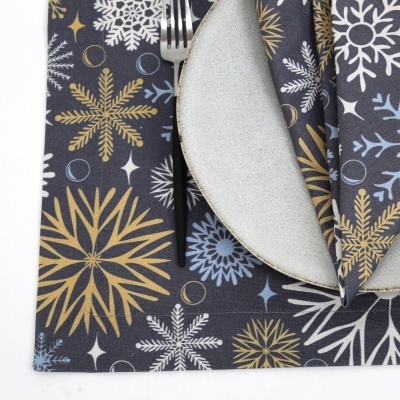 Guardanapo e toalha de mesa com padrão de flocos de neve e prato cinza com garfo.