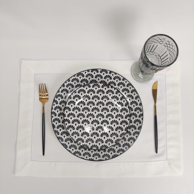 Conjunto de pratos brancos com padrão preto, talheres dourados e pretos e copo decorado sobre individual branco