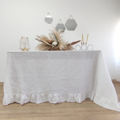 Mesa com toalha branca com babado e decoração de flores secas, castiçais dourados e espelhos hexagonais na parede