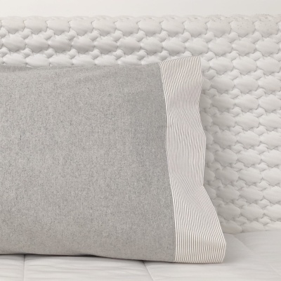 Almofada cinzenta com borda riscada branca e cinzenta sobre superfície branca texturada