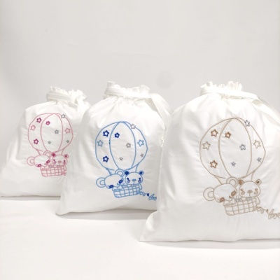 Três saquinhos brancos com bordados de balão de ar quente e ursinhos em rosa, azul e bege