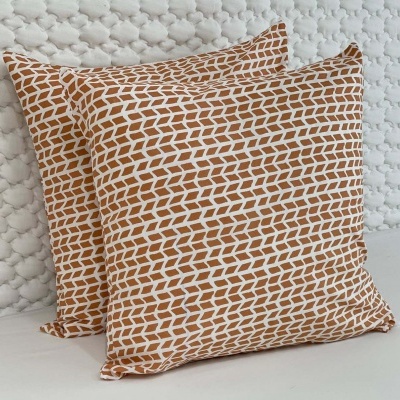 Duas almofadas com padrão geométrico castanho e branco sobre almofadas brancas texturizadas