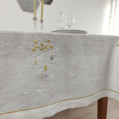 Toalha de mesa branca com bordado amarelo e cinza numa mesa de madeira e decoração ao fundo