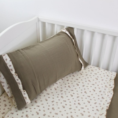 Berço branco com almofada castanha e lençol bege com padrão floral