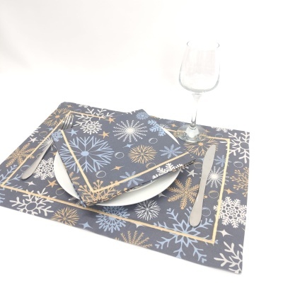 Jogo americano e guardanapo azul com flocos de neve dourados e brancos, talheres, prato branco e copo de vidro.