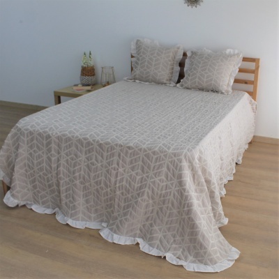 Colcha e fronhas bege com padrão geométrico branco e babado branco numa cama de madeira clara