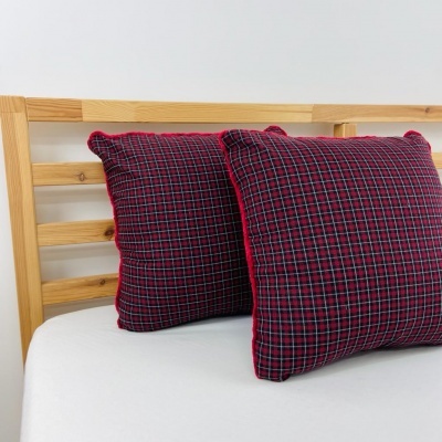 Duas almofadas quadradas com padrão de riscas vermelho, preto e branco sobre cama de madeira clara