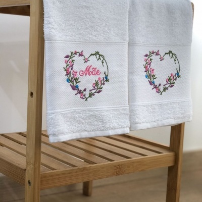 Toalhas brancas de banho com bordado floral e a palavra Mãe penduradas em estrutura de madeira