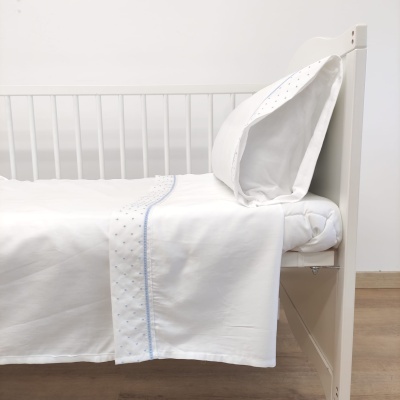 Cama branca com roupa de cama branca decorada com pontos azuis e almofada combinando.