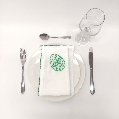 Conjunto de jantar com prato branco, guardanapo bordado verde, talheres e taça de vidro