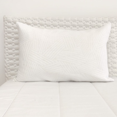 Travesseiro branco com padrão texturizado geométrico numa cama com cabeceira acolchoada branca