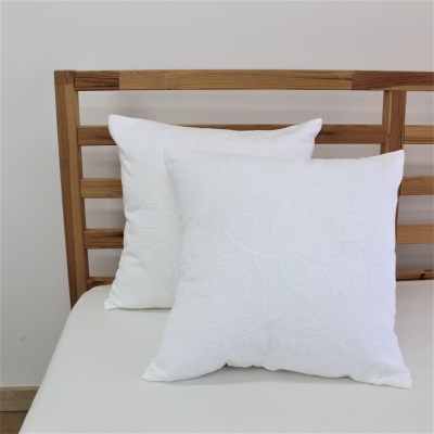Duas almofadas brancas com padrão floral em relevo numa cama com lençol branco e cabeceira de madeira