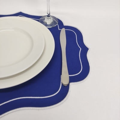 Conjunto de mesa com placa azul, prato branco, faca inox e taça sobre superfície branca