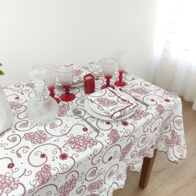 Mesa com toalha branca com padrão vermelho, loiças, copos de vidro e cortinas brancas