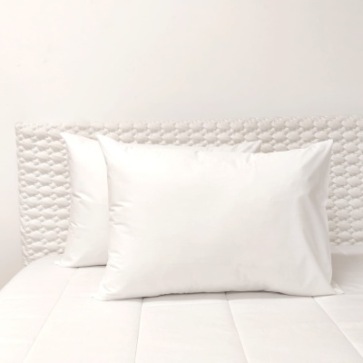 Três almofadas brancas sobre cama e cabeceira branca texturizada