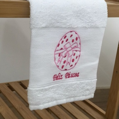 Toalha branca bordada com ovo e texto Feliz Páscoa pendurada em estrutura de madeira