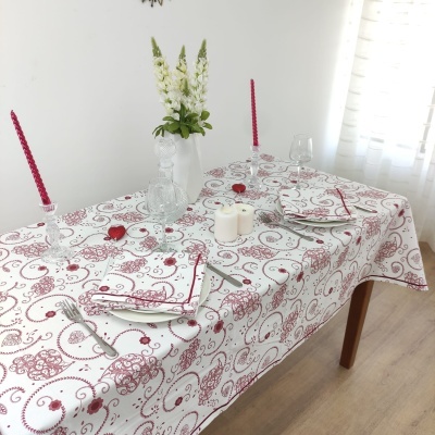 Mesa de jantar com toalha branca e arabescos vermelhos, flores e velas
