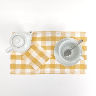 Conjunto de chá branco em porcelana com colher sobre individual e guardanapo xadrez amarelo e branco