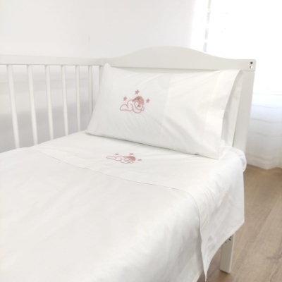 Conjunto de roupa de cama branco para berço com bordados cor-de-rosa em berço branco num quarto claro