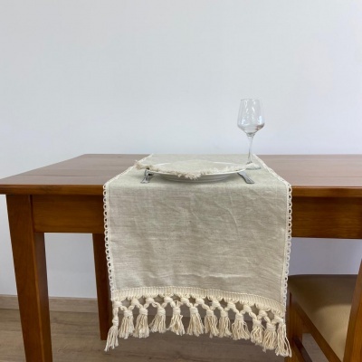 Caminho de mesa bege claro com franjas em mesa de madeira com prato, talheres e copo