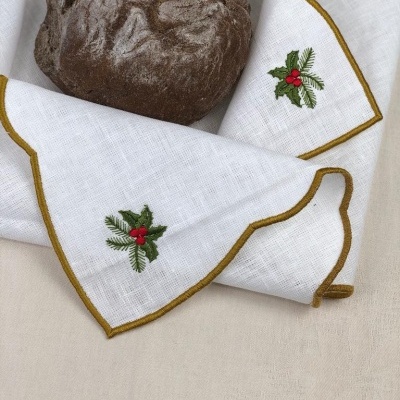 Pano de cozinha branco com bordados de folhas e frutos, envolvendo pão castanho.