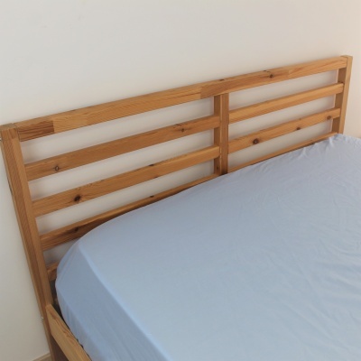 Cama de madeira clara com cabeceira em ripas e colchão com lençol azul