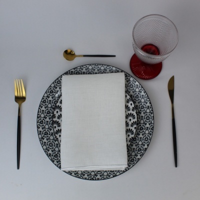 Conjunto de jantar com pratos decorados, talheres preto e dourado e copo de vidro com base vermelha