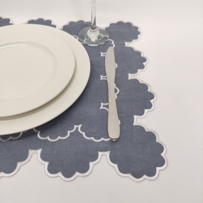 Jogo americano cinzento com bordas brancas, faca de metal e pratos brancos sobre mesa branca