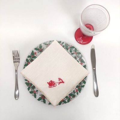 Mesa posta com prato decorado, guardanapo branco com bordado vermelho, talheres prateados e copo com base vermelha