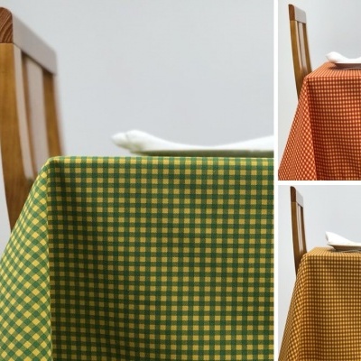 Toalhas de mesa xadrez verde, laranja e castanho sobre mesas com cadeiras de madeira