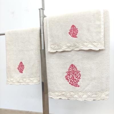 Conjunto de toalhas bege com bordado vermelho e barra em renda numa barra metálica