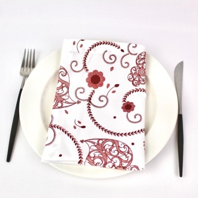Guardanapo branco com padrão floral vermelho sobre prato branco, garfo e faca com cabo preto
