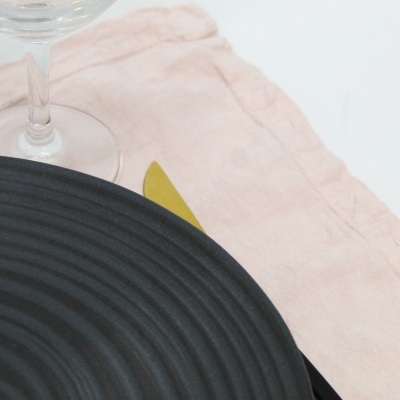 Prato preto texturizado com guardanapo rosa, faca dourada e copo de vidro.