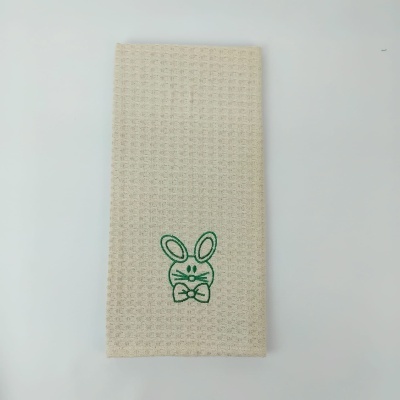 Toalha bege claro texturizada com bordado de coelho verde.