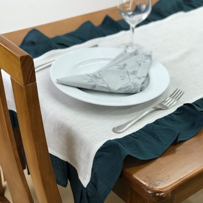 Mesa posta com toalha branca com borda azul escura, prato branco, guardanapo cinza estampado e copo de vidro