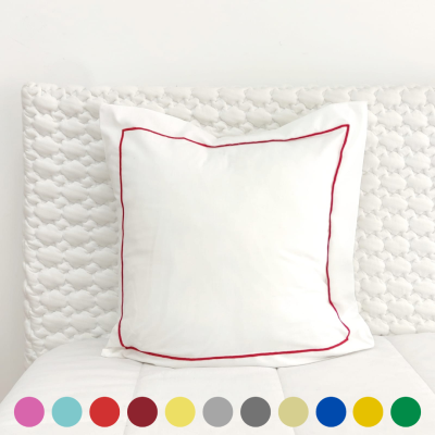 Almofada branca com borda vermelha numa cama branca com cabeceira estofada