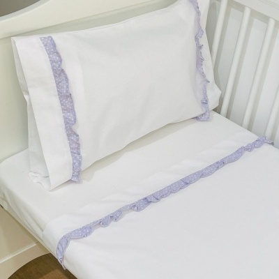 Lençol e fronha brancos com babados lilás de pequenos pontos em berço branco