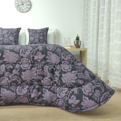 Edredão e almofadas com padrão floral roxo e preto numa cama em quarto com decoração simples.
