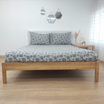 Cama de madeira clara com roupa de cama cinza com padrão floral e cabeceira acolchoada branca