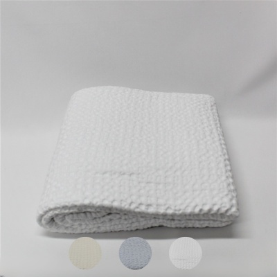 Manta branca dobrada com textura de colmeia em fundo claro e círculos de cores abaixo