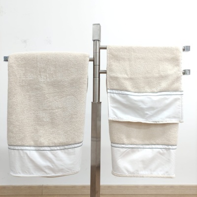 Toalhas de banho e rosto bege com bainha branca penduradas em suporte metálico