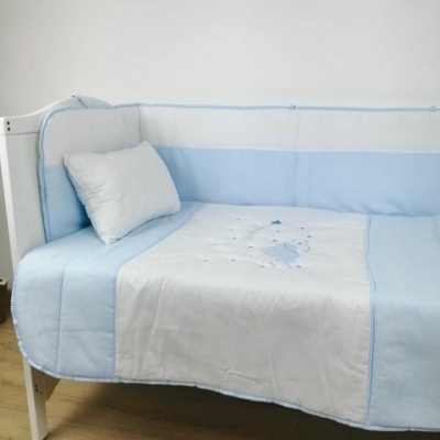 Berço com edredão azul claro e branco com bordado de ursinho