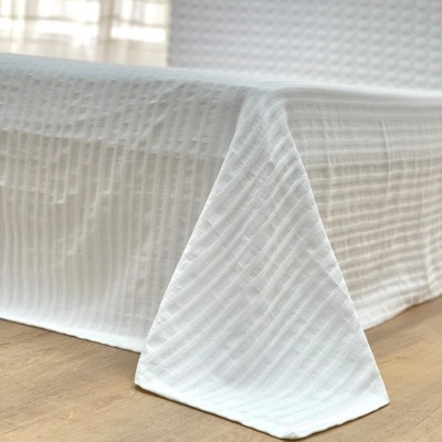 Cama com cobertura branca texturizada padrão reticulado em quarto com chão de madeira