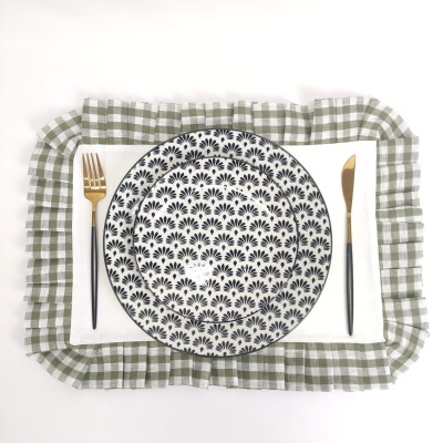 Prato de cerâmica branco com padrão floral azul escuro sobre guardanapo branco e jogo americano xadrez verde e branco com talheres