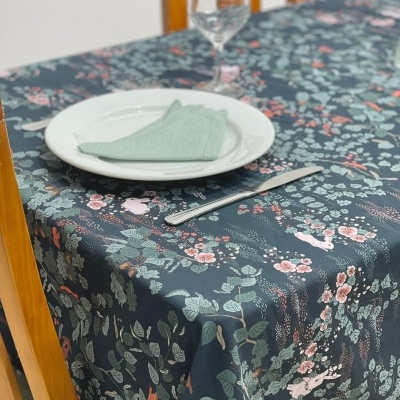 Toalha de mesa azul escura com padrão floral colocada numa mesa com prato, guardanapo verde, faca e copo.