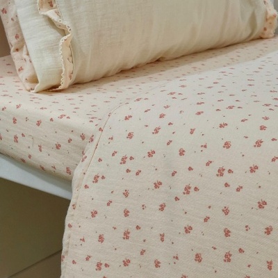 Jogo de cama em algodão creme com padrão floral rosa e folho decorativo.