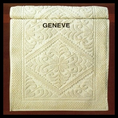 Toalha de banho creme com padrão em relevo e texto 'GENEVE' impresso