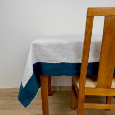 Toalha de mesa cinzento claro com borda azul escuro numa mesa de madeira com cadeira