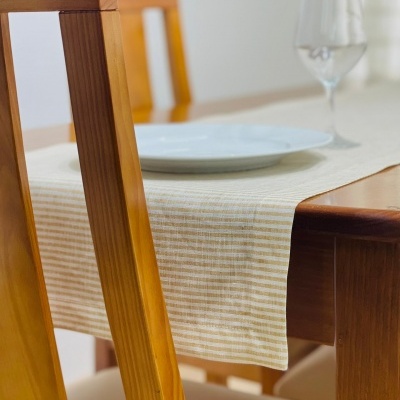 Mesa de madeira com toalha bege, prato branco e copo de vidro