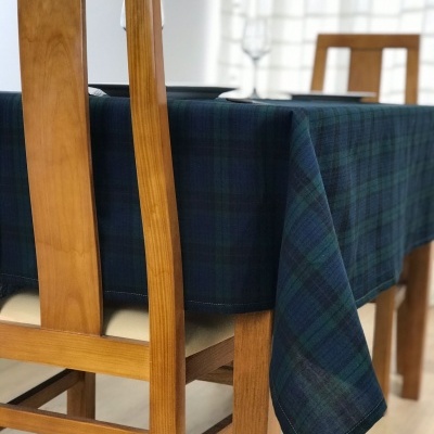 Toalha de mesa xadrez verde e azul em mesa de madeira clara com cadeiras e cortinas brancas